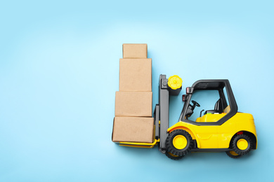 Top view of toy forklift with boxes on blue background, space for text. Logistics and wholesale concept