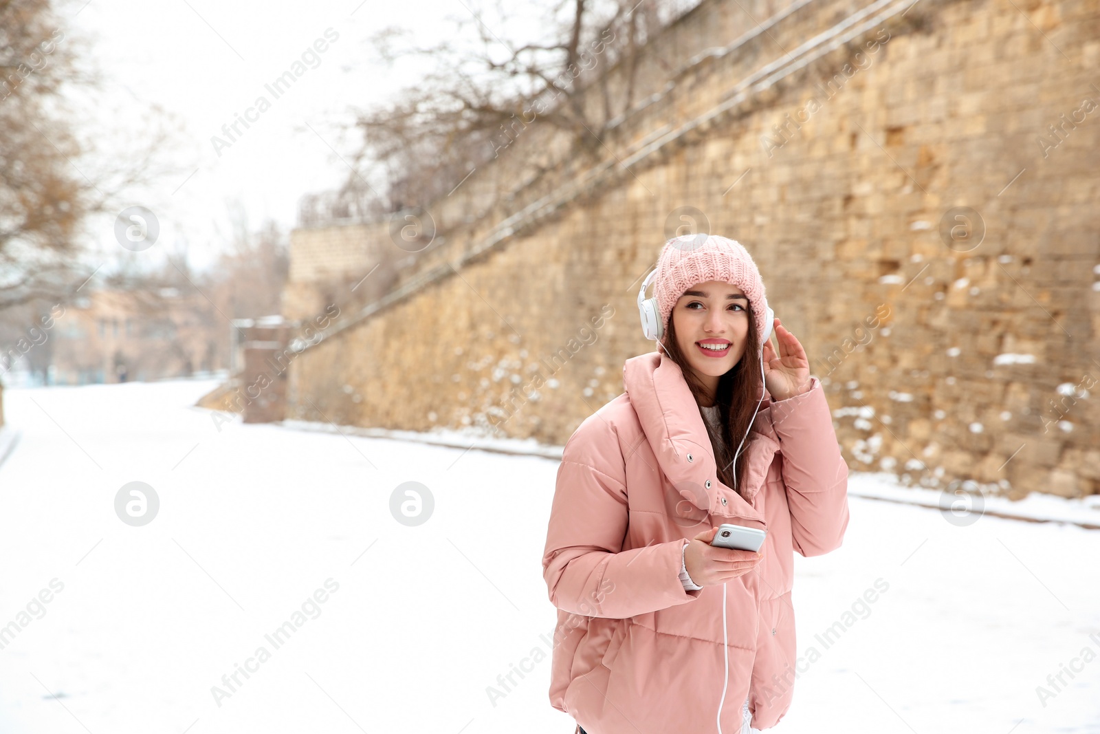 Photo of Beautiful young woman listening to music with headphones outdoors. Space for text