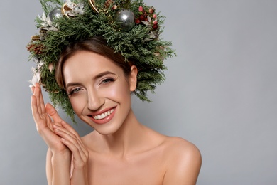 Photo of Beautiful young woman wearing Christmas wreath on grey background. Space for text