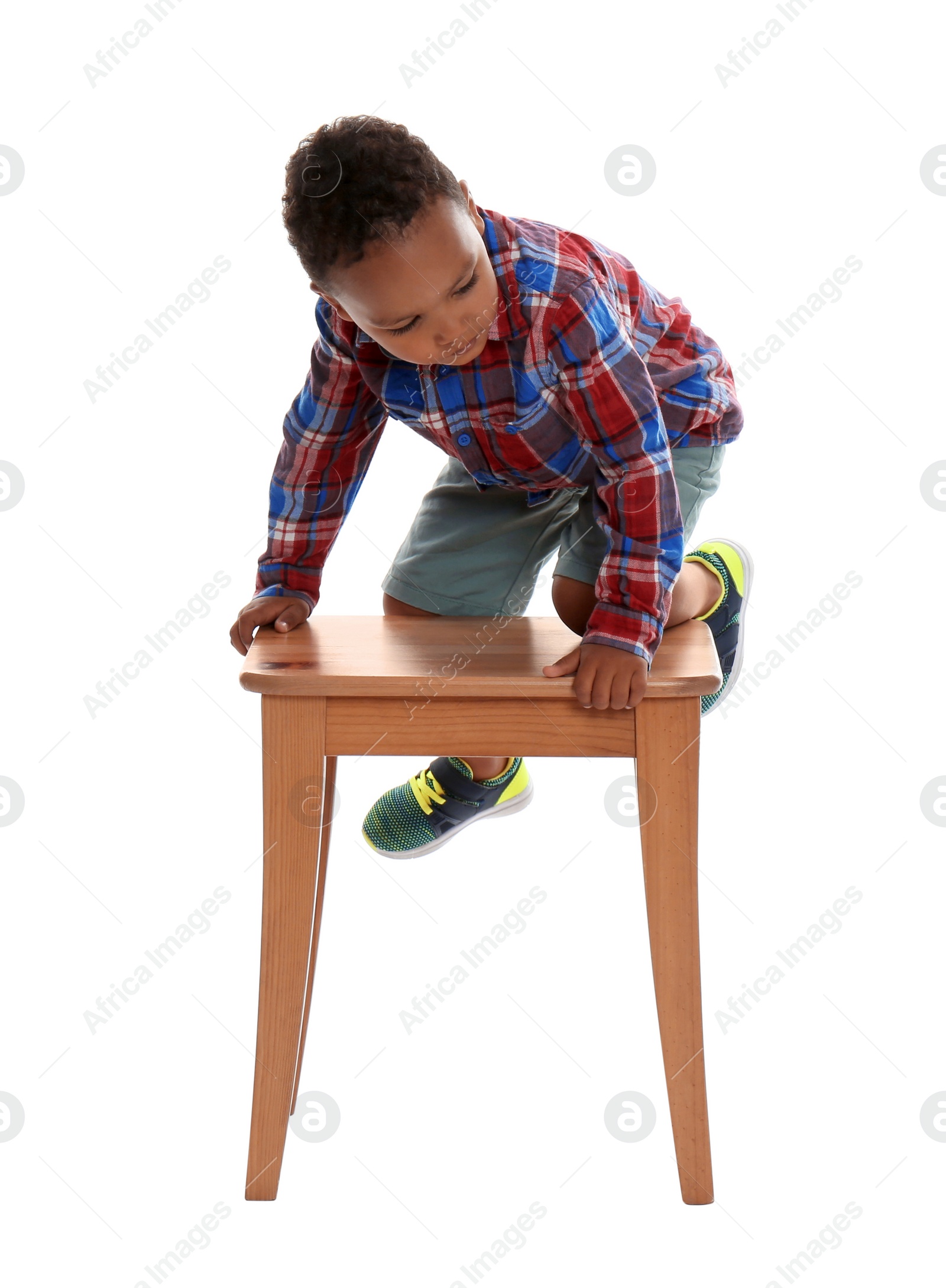 Photo of Little African-American boy climbing up stool on white background. Danger at home