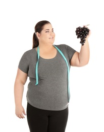 Overweight woman with grapes and measuring tape on white background
