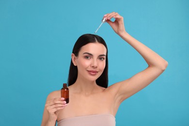 Photo of Beautiful woman applying hair serum on light blue background. Cosmetic product