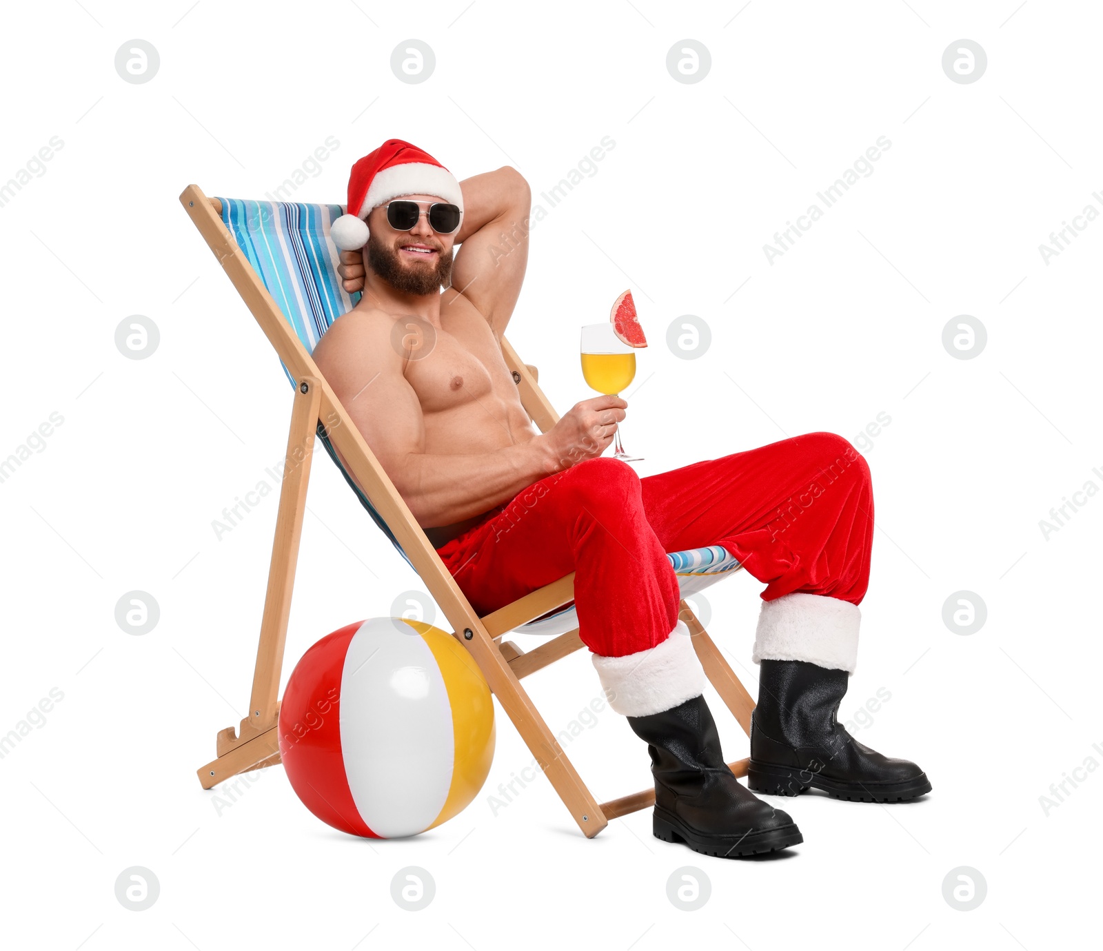 Photo of Muscular young man in Santa hat with deck chair, ball, sunglasses and cocktail on white background