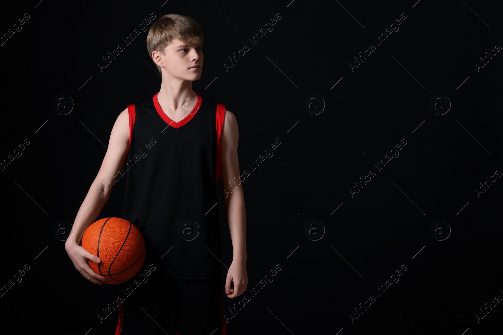 Photo of Teenage boy with basketball ball on black background. Space for text