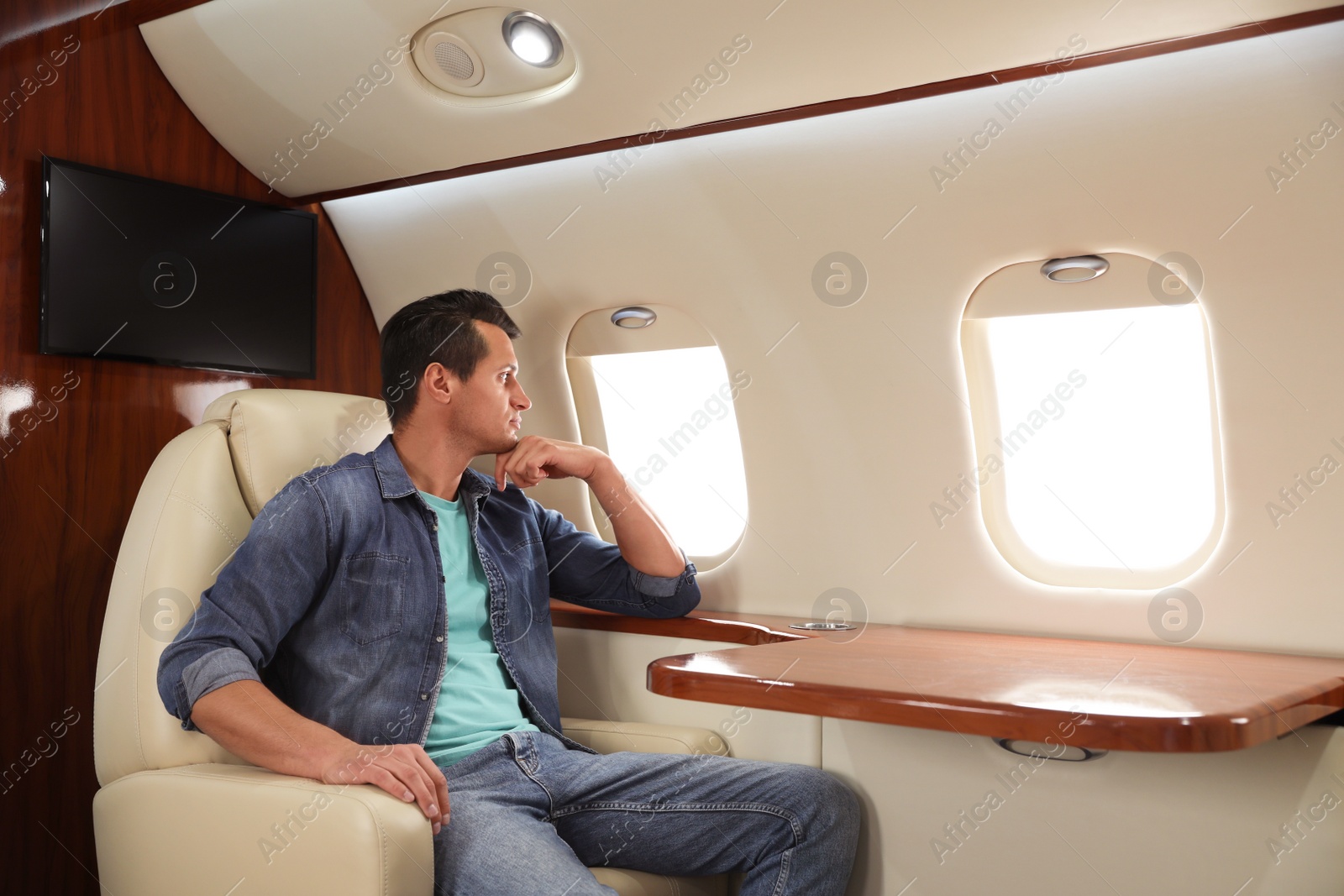 Image of Handsome man looking out of airplane window. Comfortable flight