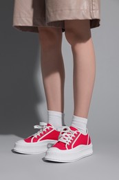 Photo of Woman wearing red classic old school sneakers on light gray background, closeup
