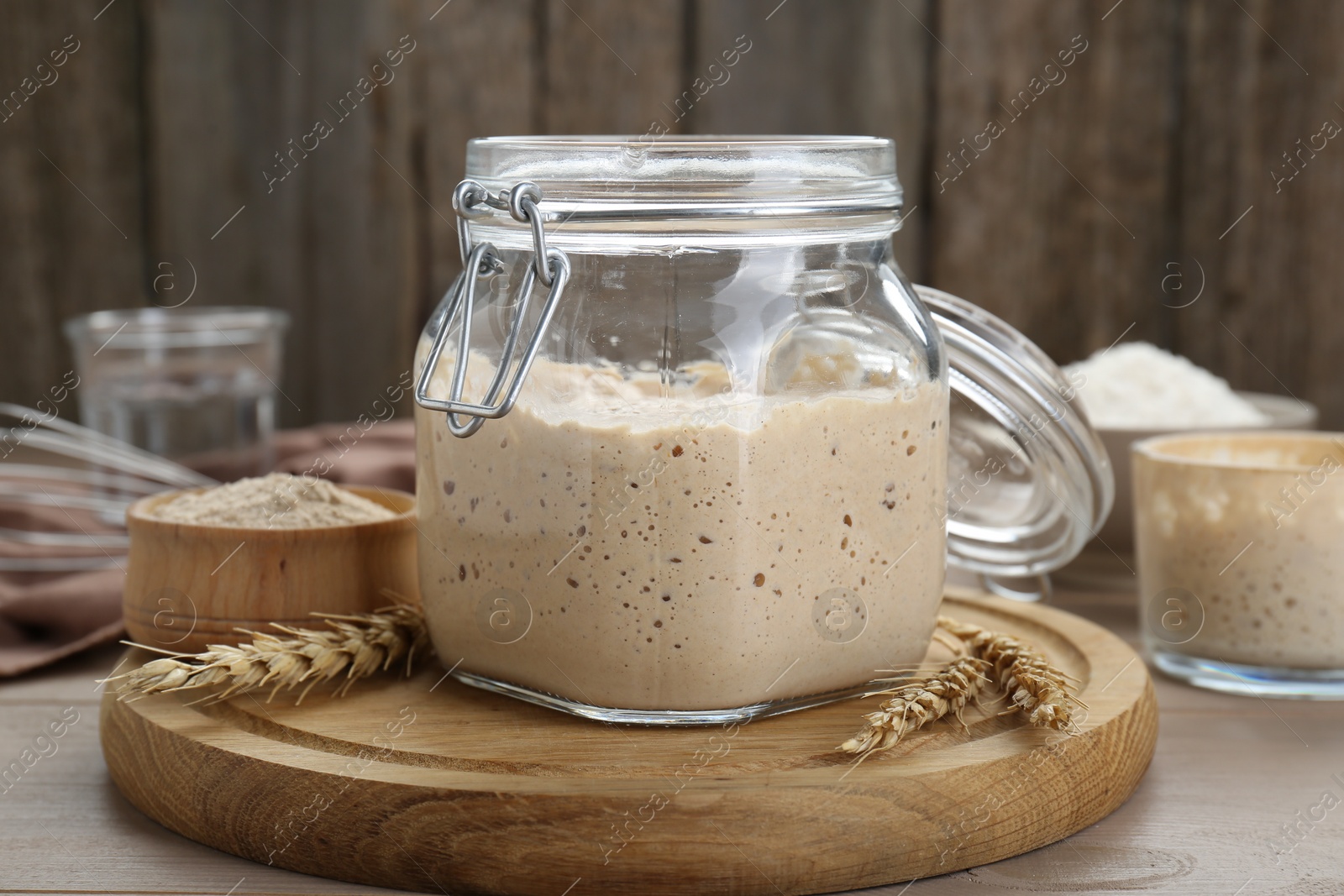 Photo of Leaven and ears of wheat on beige wooden table