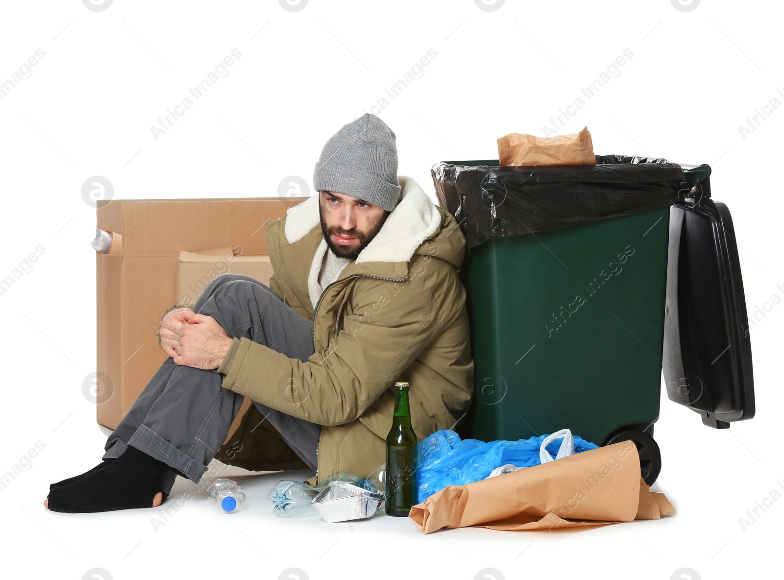 Photo of Poor homeless man sitting near trash bin isolated on white