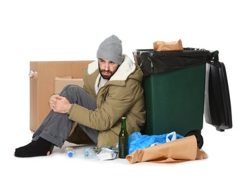 Poor homeless man sitting near trash bin isolated on white