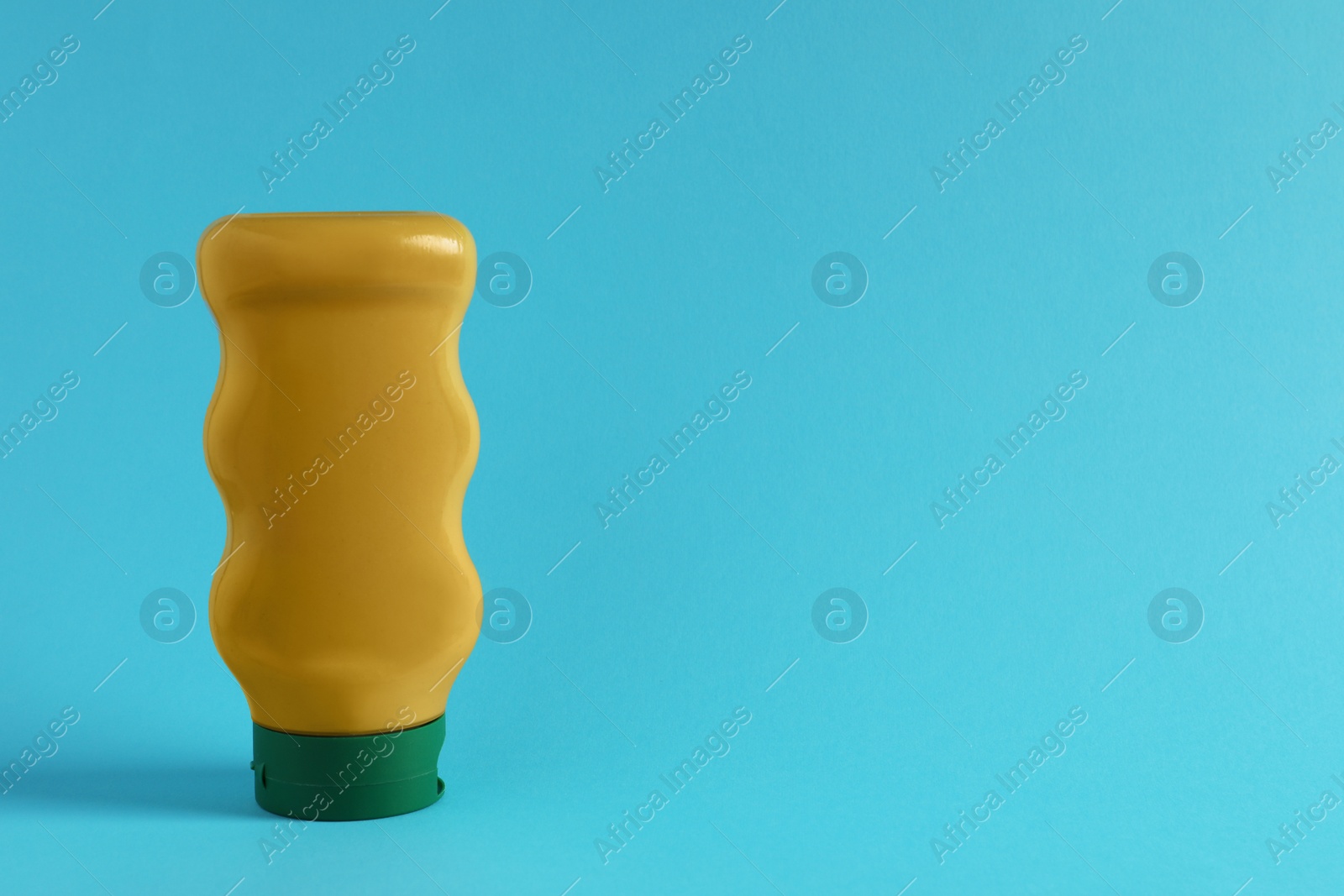 Photo of Spicy mustard in plastic bottle on light blue background, space for text