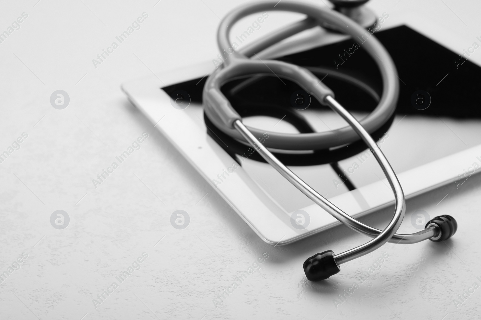 Photo of Computer tablet with stethoscope on white table, closeup. Space for text