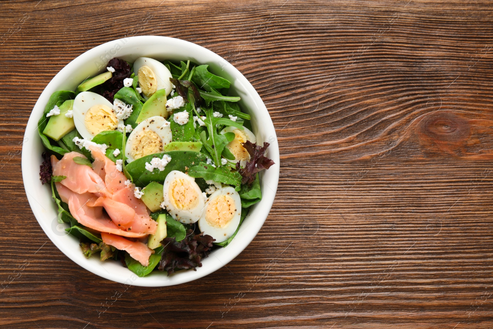 Photo of Delicious salad with boiled eggs, salmon and cheese in bowl on wooden table, top view. Space for text