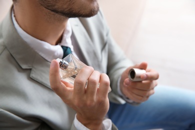 Businessman applying perfume on blurred background, closeup