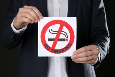 Photo of Woman holding card with no smoking sign on black background, closeup