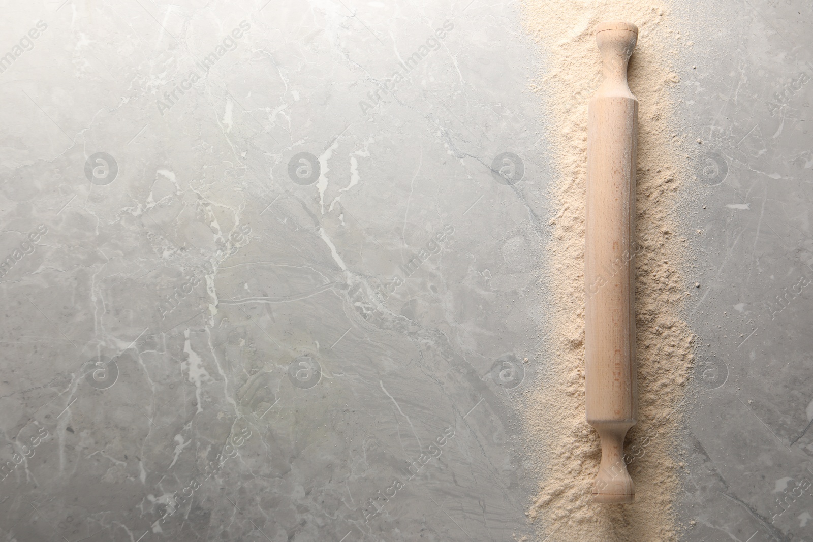 Photo of Flour and rolling pin on grey marble table, top view. Space for text