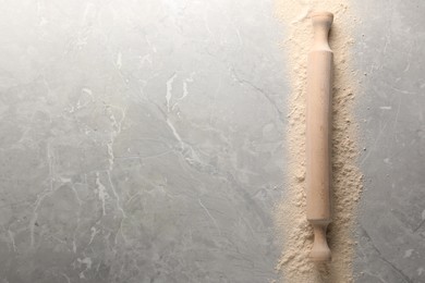 Photo of Flour and rolling pin on grey marble table, top view. Space for text