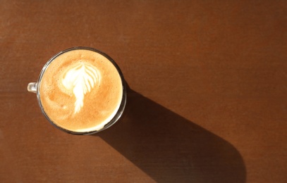 Photo of Cup of aromatic coffee with foam on wooden table, top view