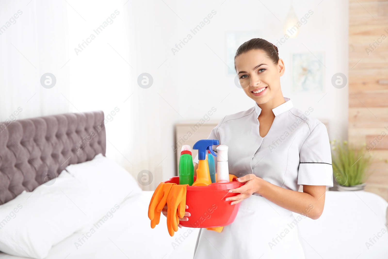 Photo of Young chambermaid with cleaning supplies in bedroom. Space for text