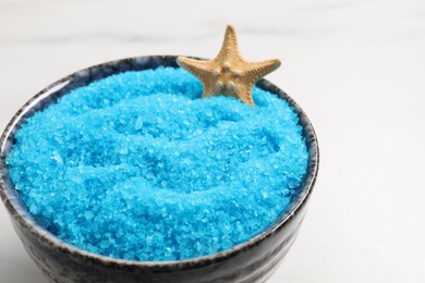 Light blue sea salt and starfish in bowl on white table, closeup. Space for text