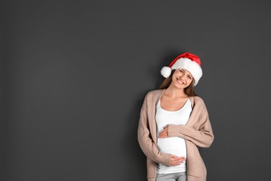 Young pregnant woman in Santa hat on grey background, space for text. Christmas celebration