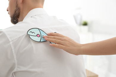 Woman sticking paper fish to colleague's back in office, closeup. April fool's day