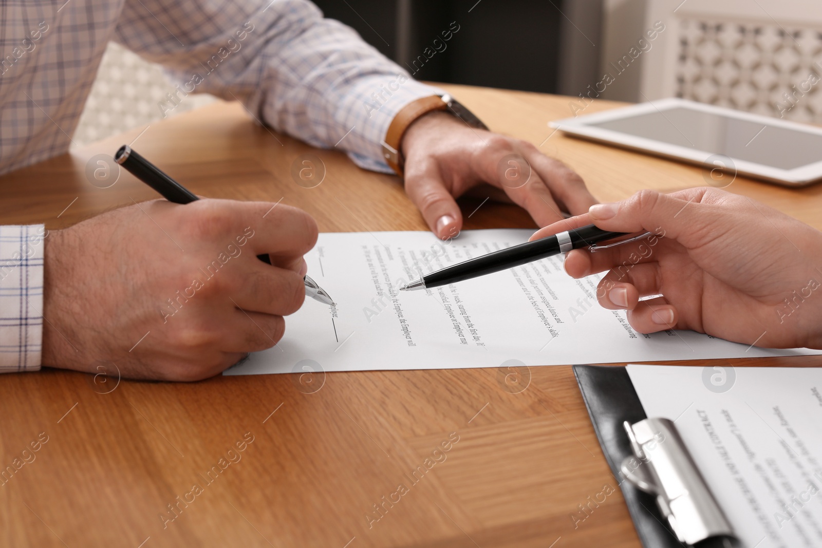 Photo of Businesspeople signing contract at wooden table indoors, closeup of hands