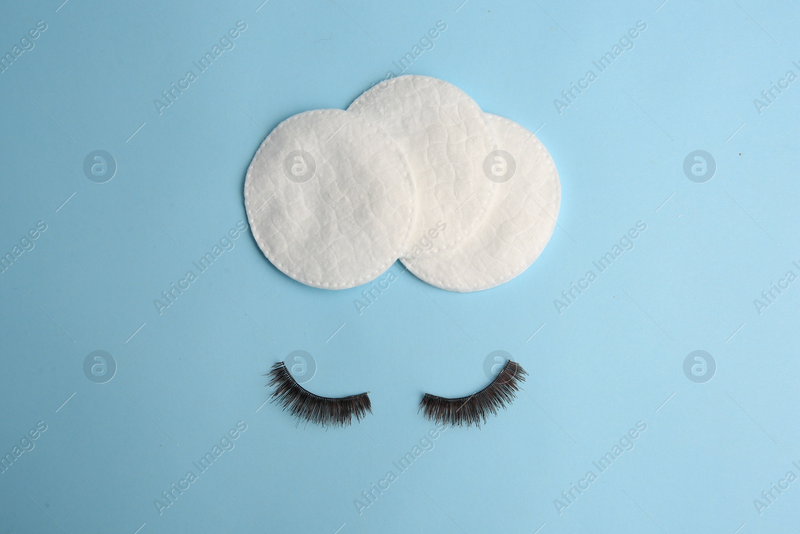 Photo of Cotton pads for makeup removal and false eyelashes on light blue background, flat lay