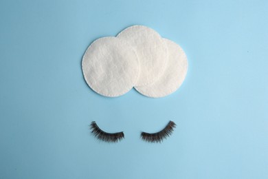 Cotton pads for makeup removal and false eyelashes on light blue background, flat lay