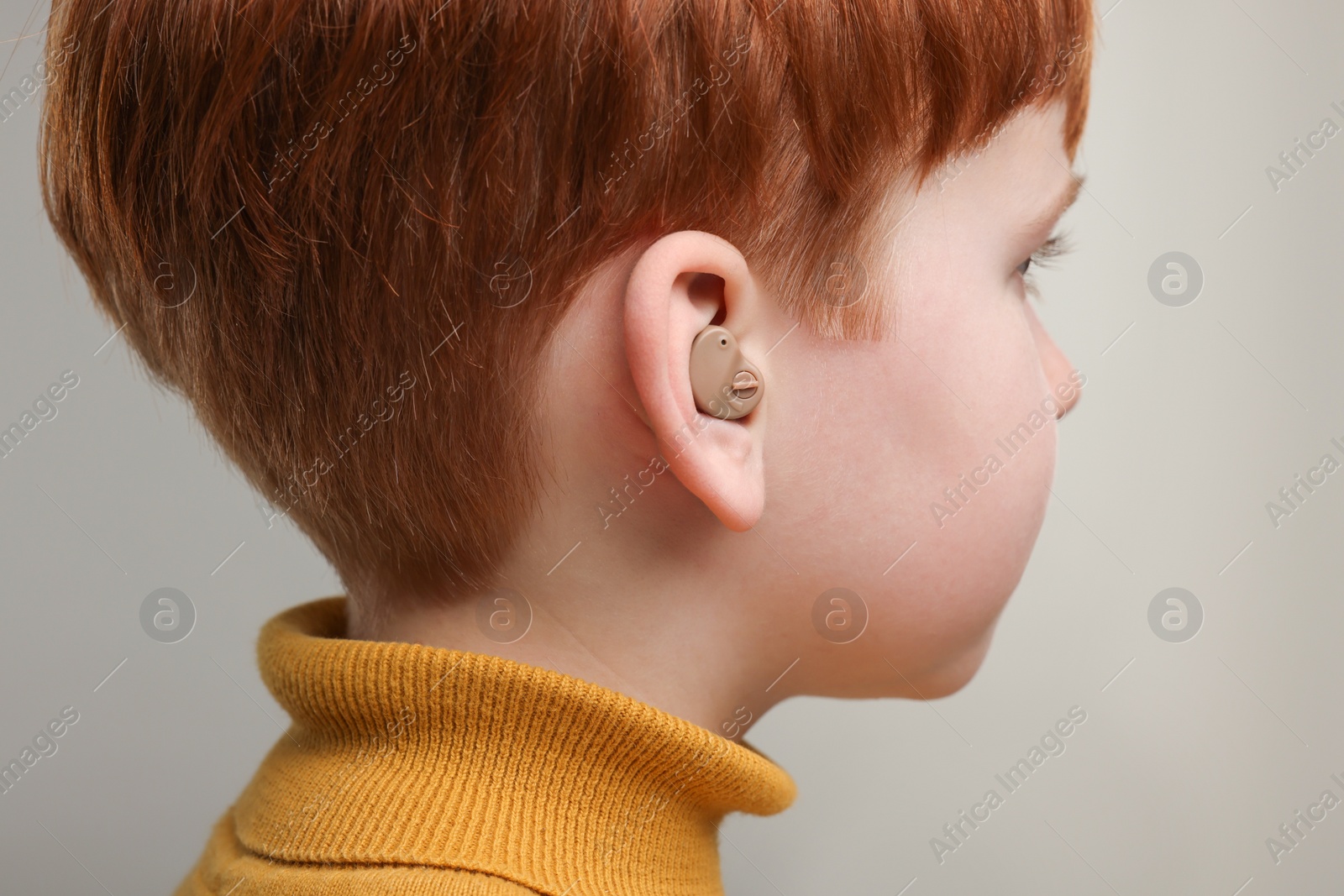 Photo of Little boy with hearing aid on grey background, closeup