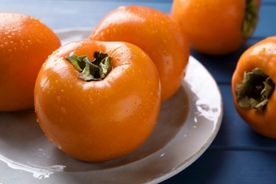 Photo of Delicious ripe persimmons on blue wooden table , closeup