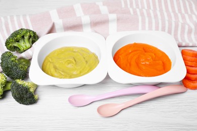 Containers with healthy baby food, spoons and ingredients on white wooden table