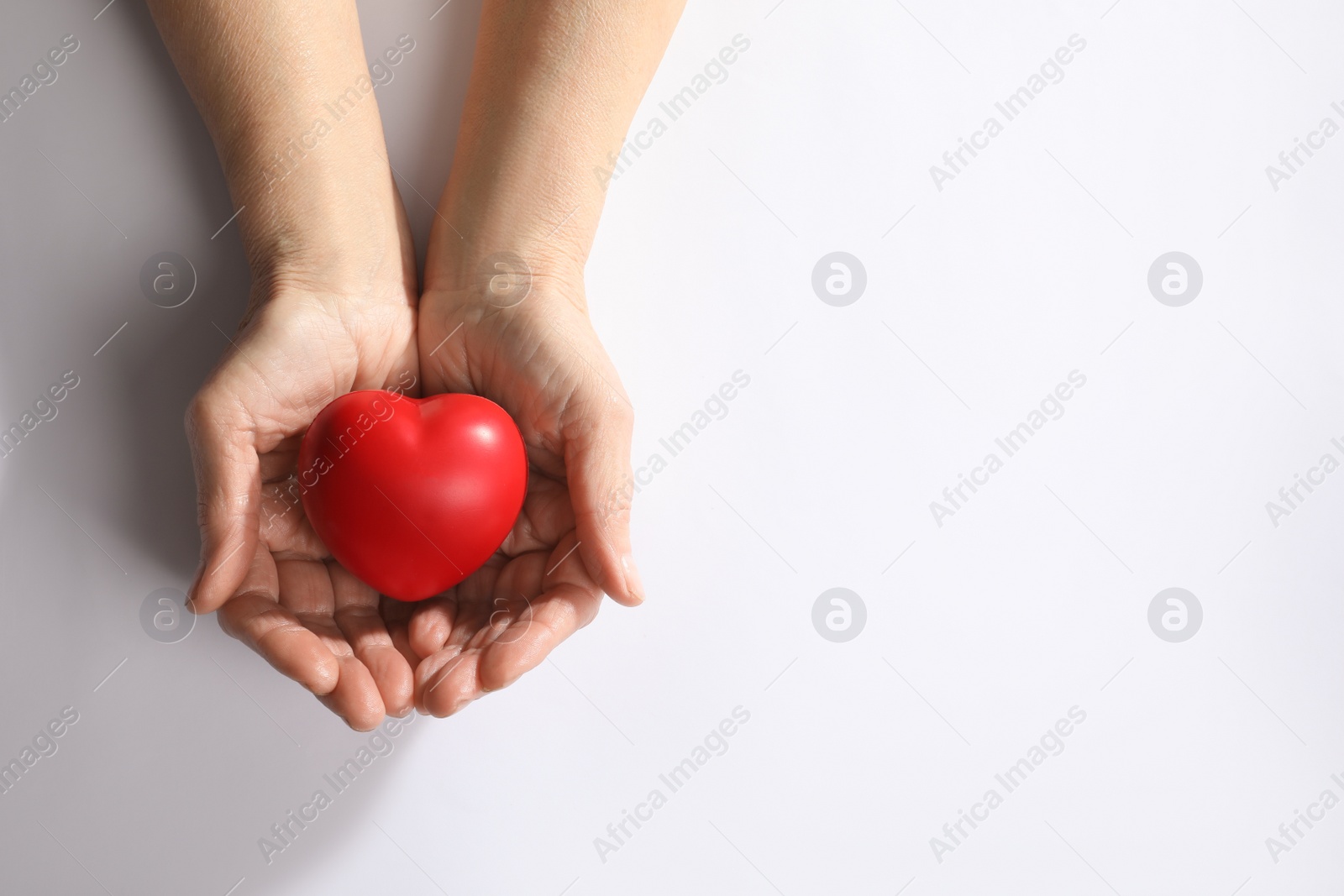 Photo of Elderly woman holding red heart in hands on white background, top view