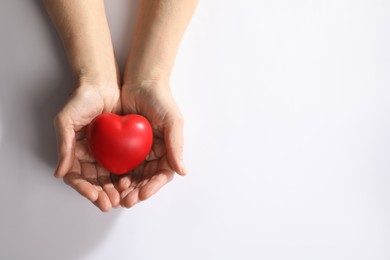 Elderly woman holding red heart in hands on white background, top view