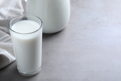 Photo of Glass and jug with fresh milk on grey table. Space for text