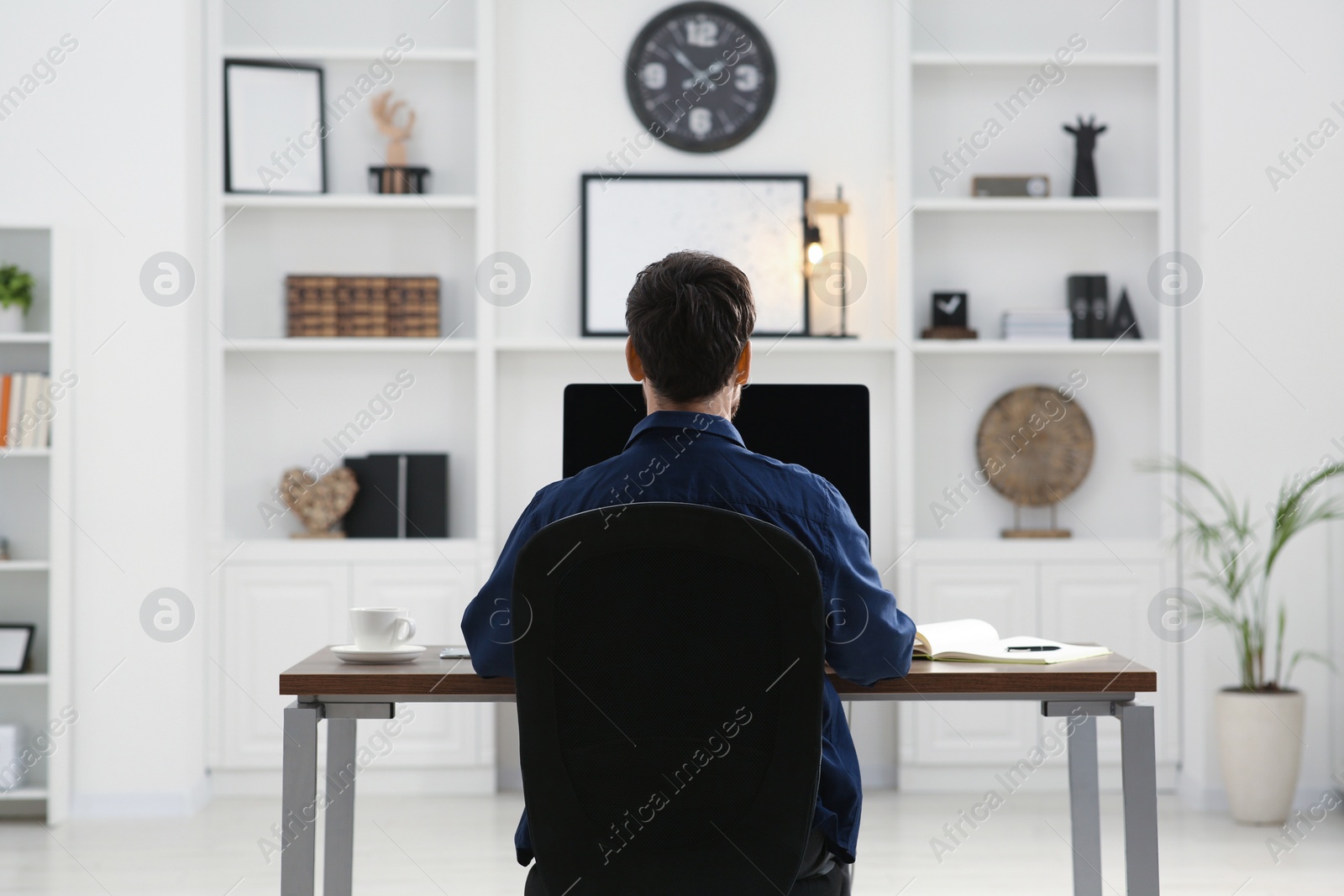 Photo of Home workplace. Man working at wooden desk in room, back view