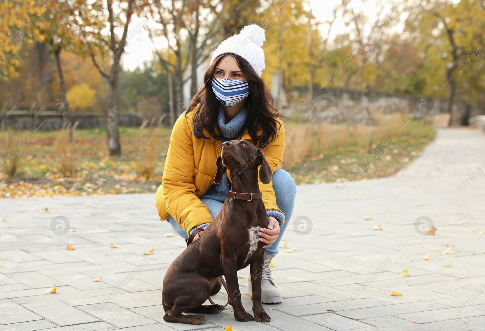 Photo of Woman in protective mask with German Shorthaired Pointer in park. Walking dog during COVID-19 pandemic