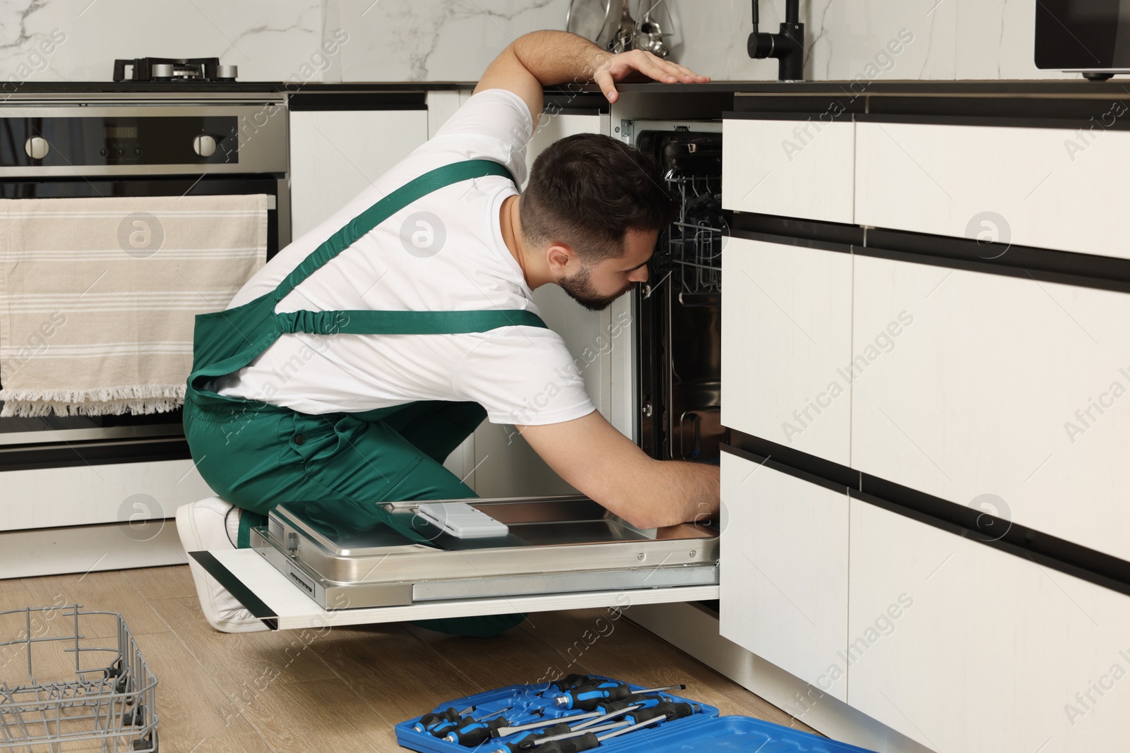 Photo of Serviceman repairing dishwasher near toolbox in kitchen