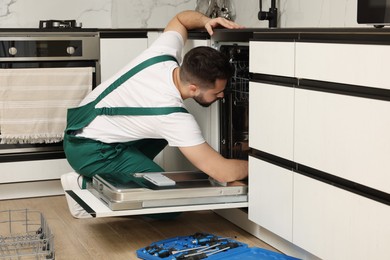 Serviceman repairing dishwasher near toolbox in kitchen