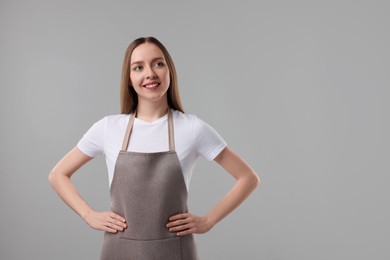 Beautiful young woman wearing kitchen apron on grey background. Mockup for design