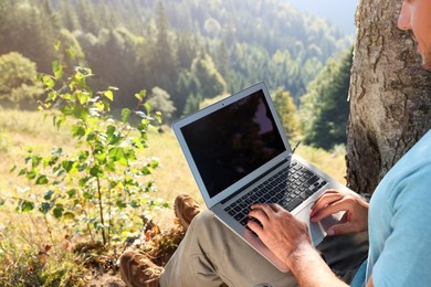 Photo of Man working on laptop outdoors surrounded by beautiful nature, closeup. Space for text