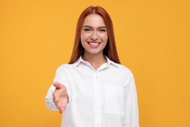 Photo of Happy woman welcoming and offering handshake on orange background