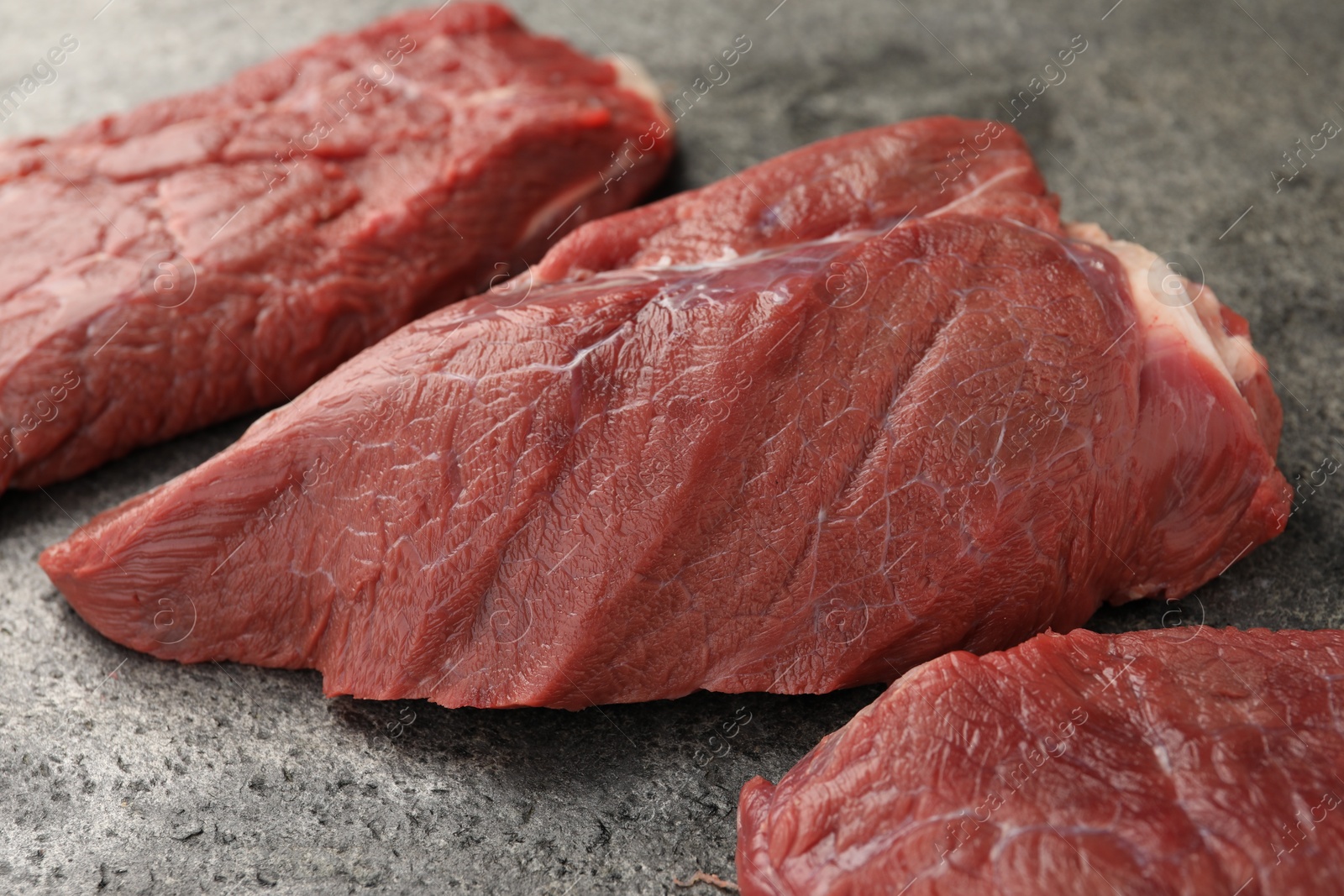 Photo of Pieces of raw beef meat on grey table, closeup