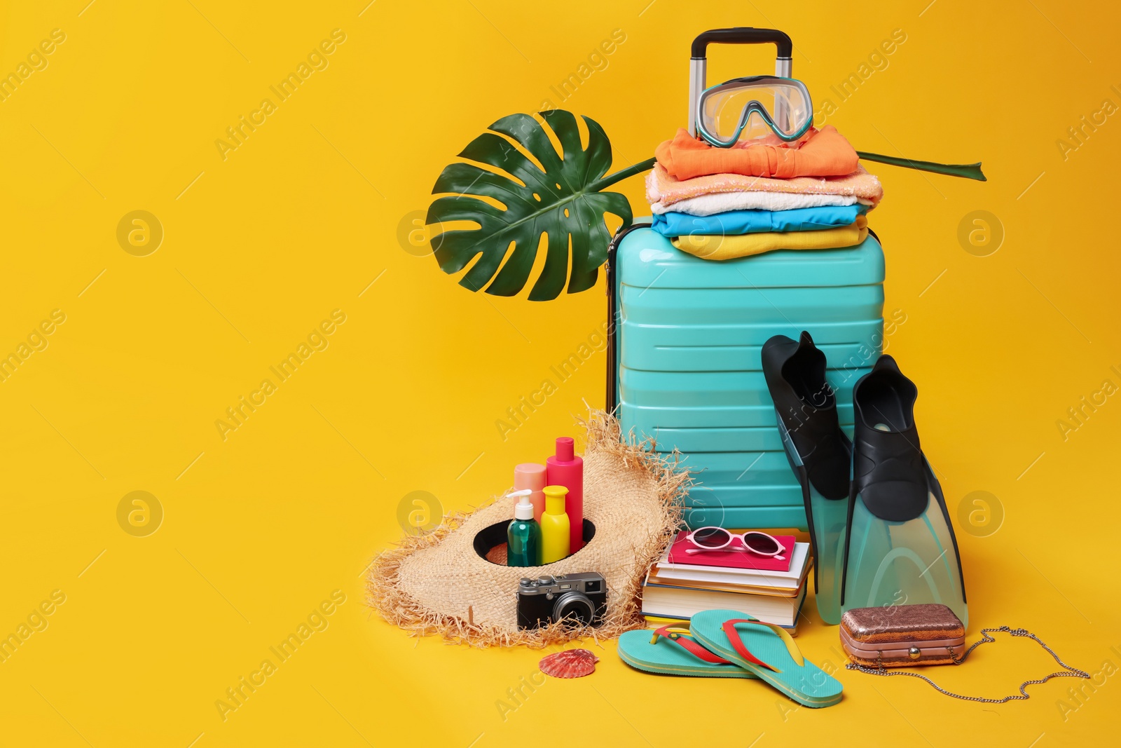 Photo of Suitcase, clothes and beach accessories on yellow background, space for text. Summer vacation