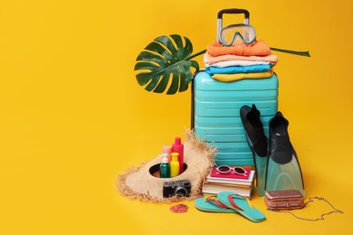 Suitcase, clothes and beach accessories on yellow background, space for text. Summer vacation