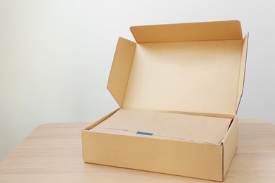 Photo of Open cardboard box with item wrapped in kraft paper on wooden table, space for text. Delivery service