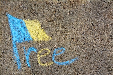Photo of National flag of Ukraine with word Free drawn by blue and yellow chalk on asphalt, top view