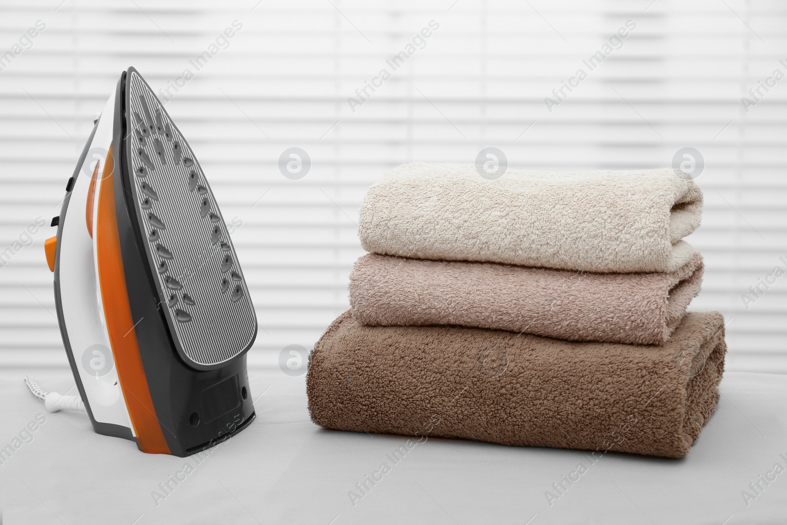 Photo of Modern iron and clean towels on board near blinds