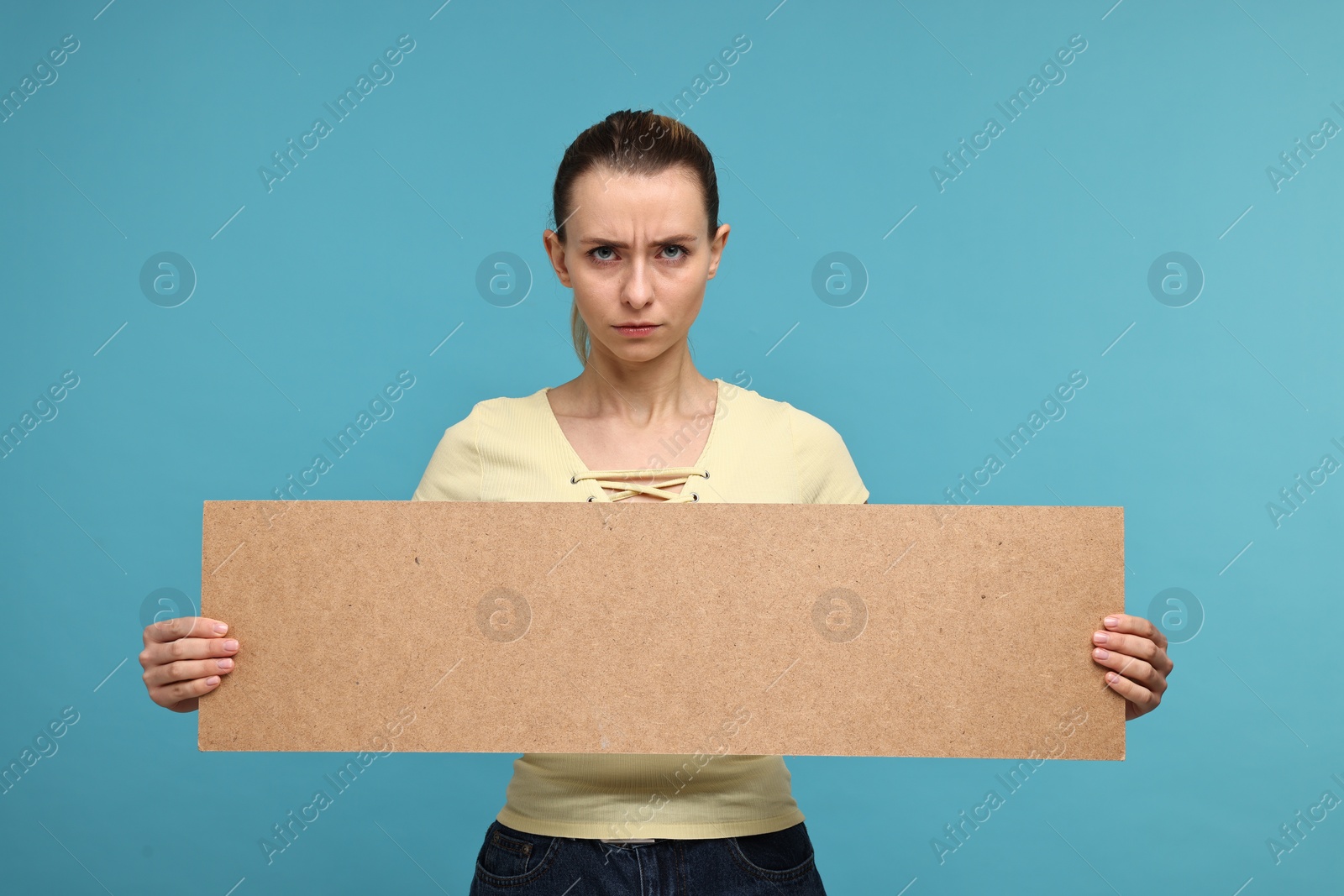 Photo of Upset woman holding blank cardboard banner on light blue background, space for text