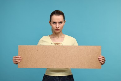 Upset woman holding blank cardboard banner on light blue background, space for text