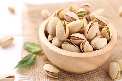 Tasty pistachios in bowl on white table, closeup